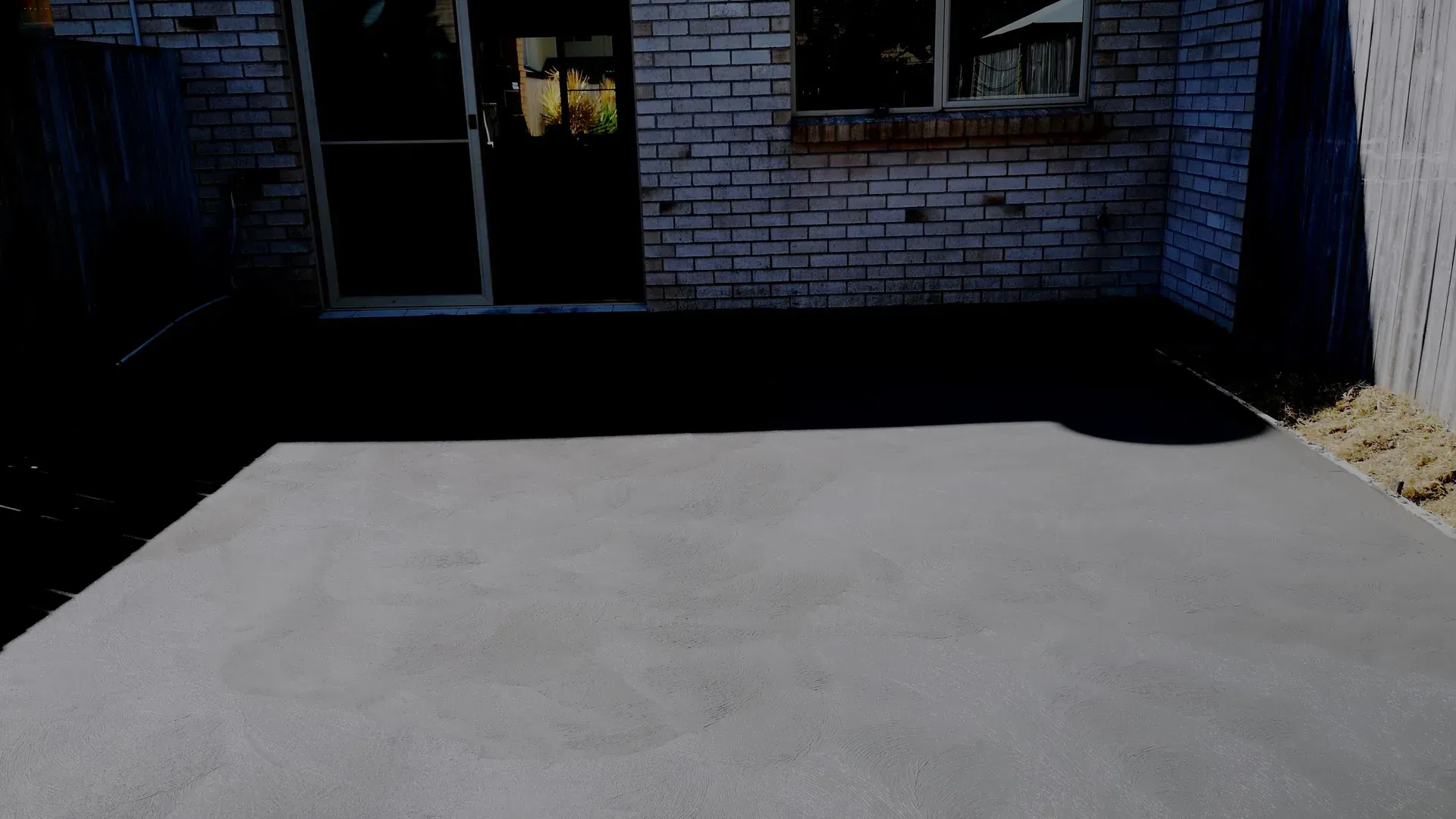 Concrete patio in front of brick wall and glass door.