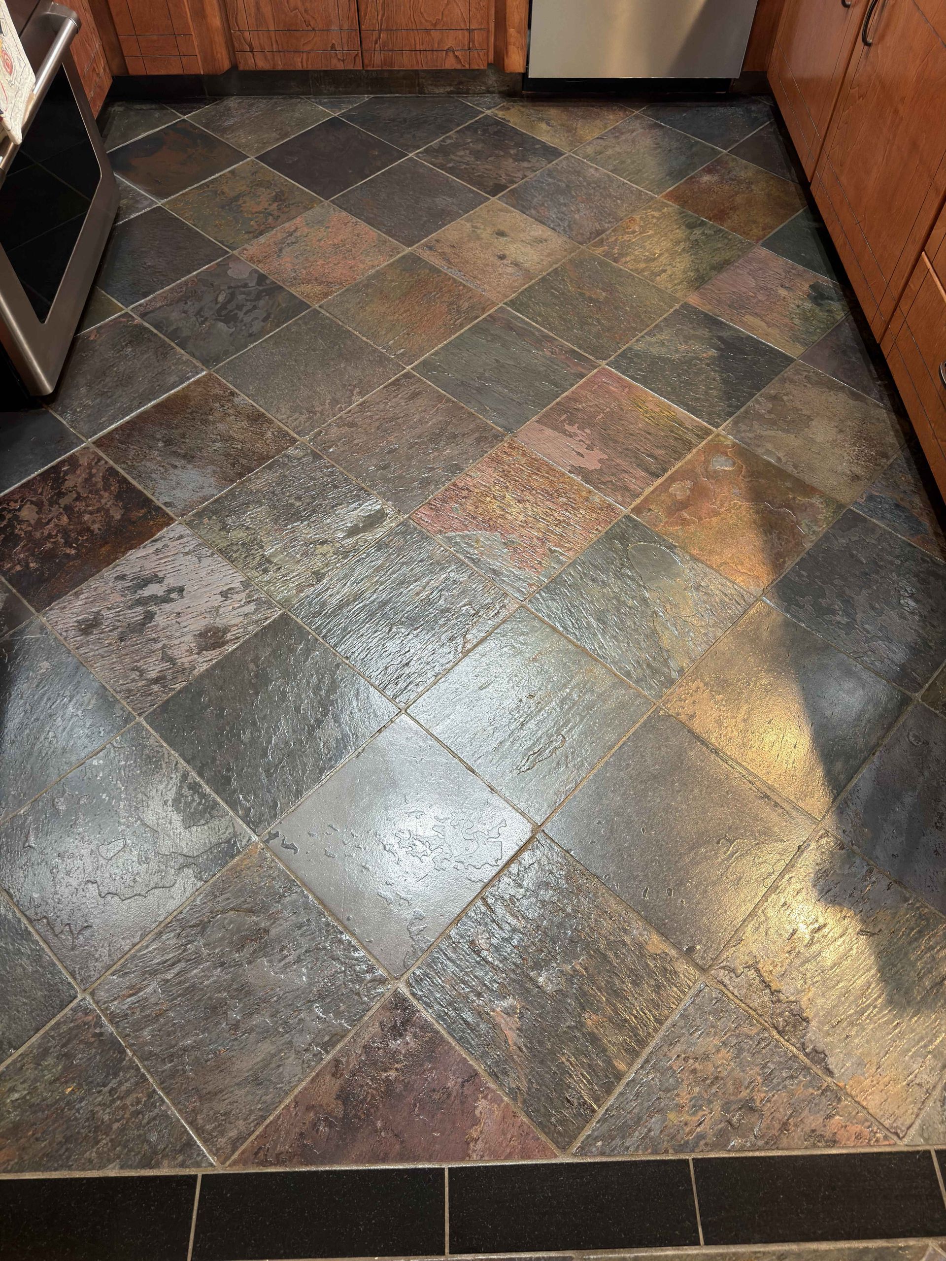 Kitchen floor with dark, diamond-patterned tile and a wet, reflective surface
