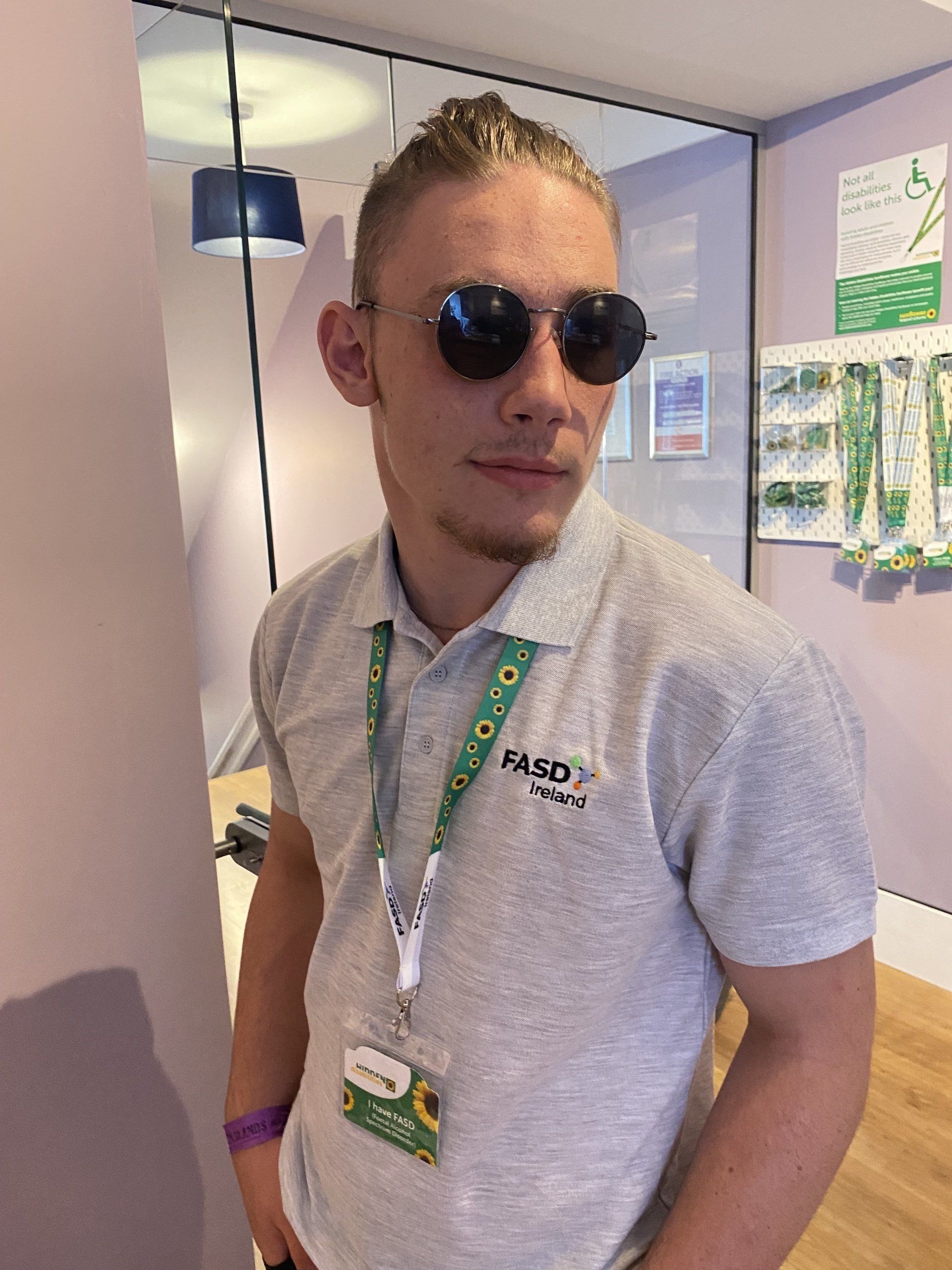 Jacob is wearing a pair of sunglasses whilst modeling an FASD Ireland Polo Shirt in the Office