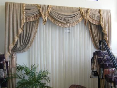 Beige and gold draped curtains over vertical blinds, showroom setting.