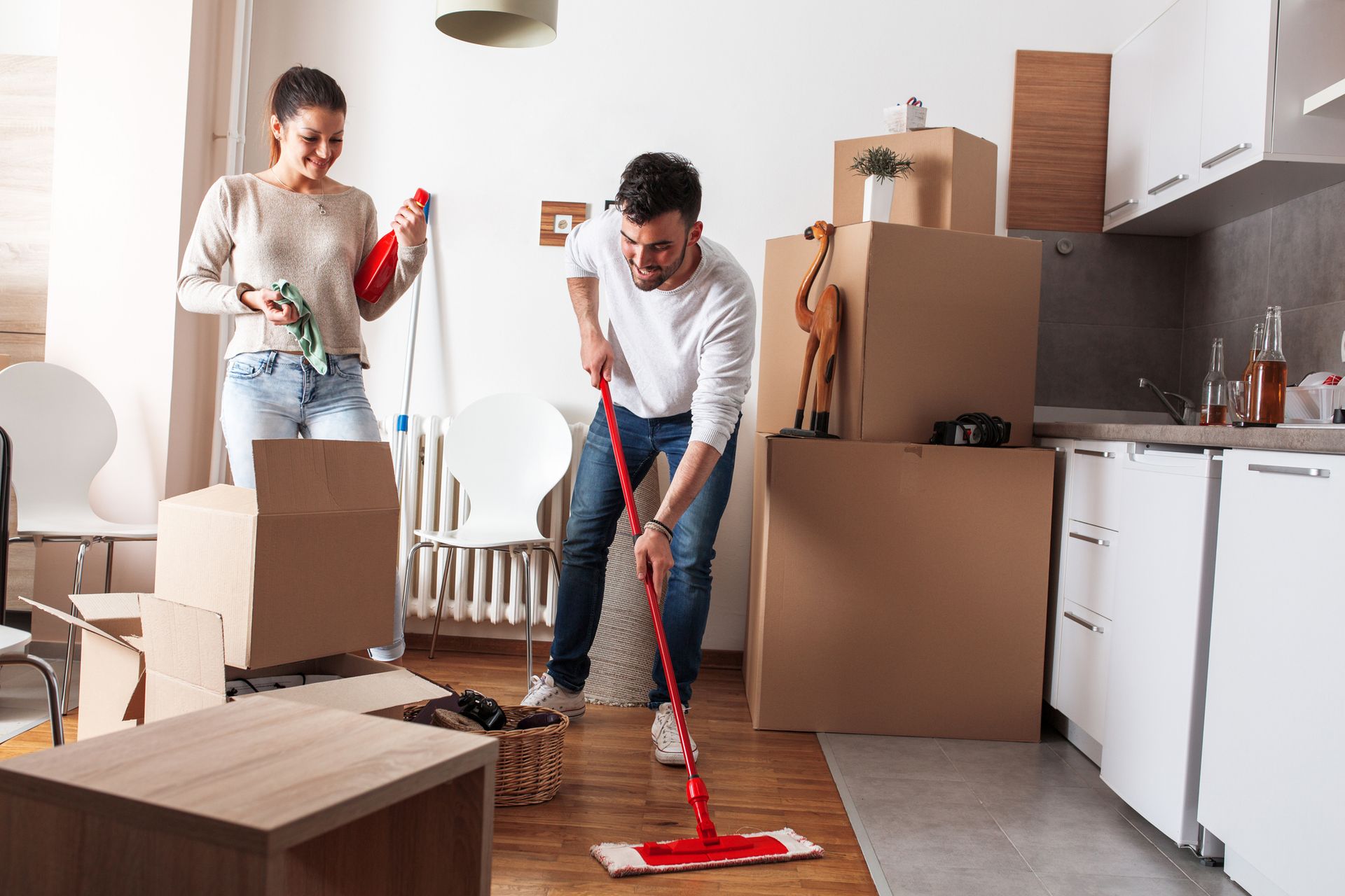 A man is mopping the floor in a kitchen while a woman stands behind him.