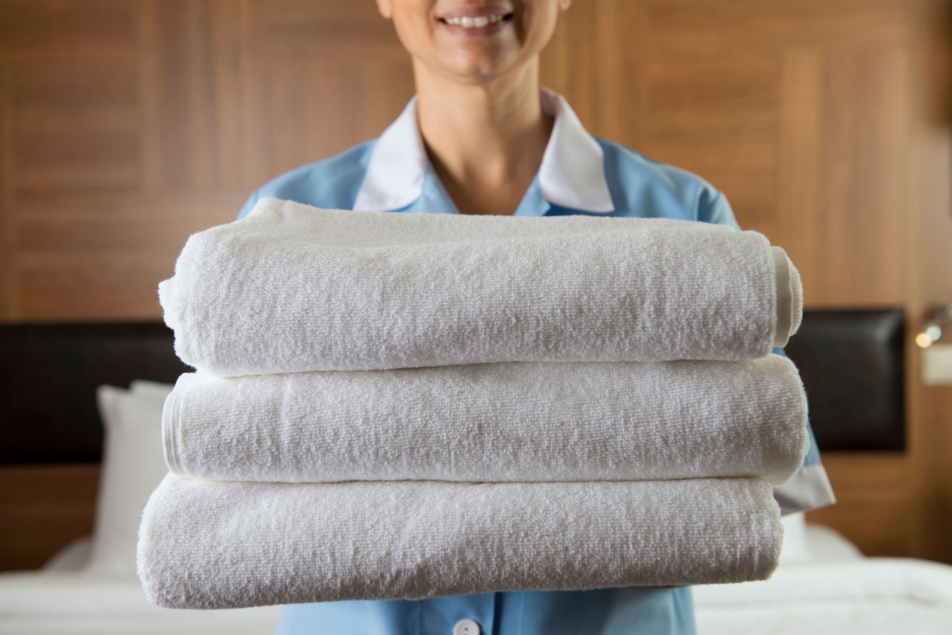 A maid is holding a stack of towels in a hotel room.