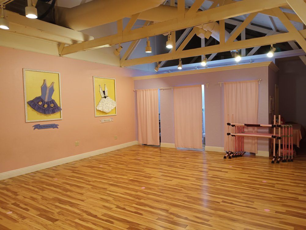 An empty dance studio with a wooden floor and pink curtains.