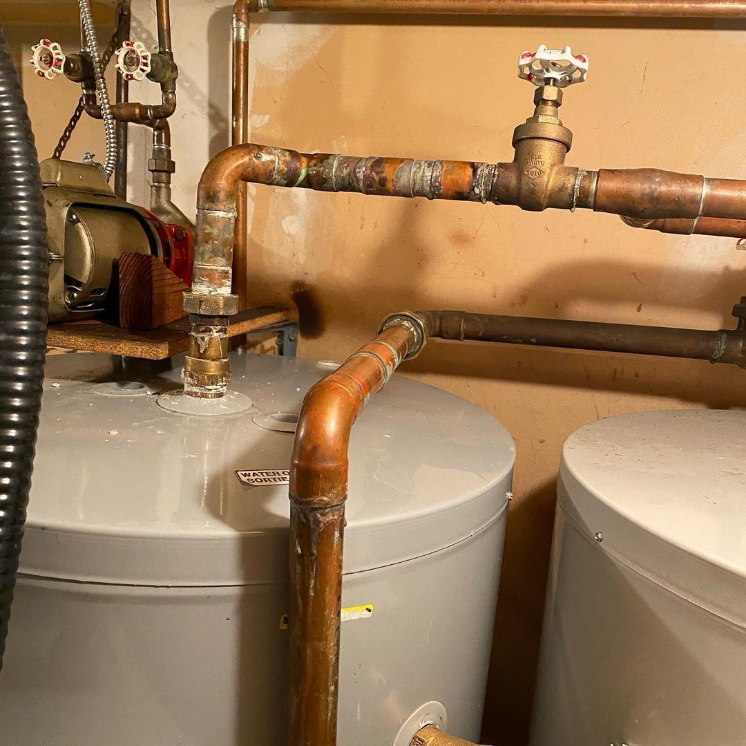 Two water heaters are sitting next to each other in a room with copper pipes.