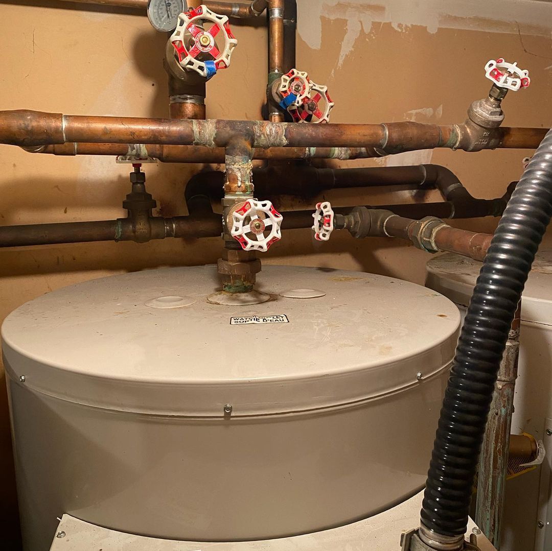 A water heater is sitting in a room surrounded by pipes and valves.