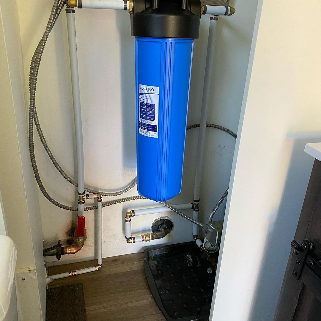 A blue water filter is hanging from a pipe in a bathroom.