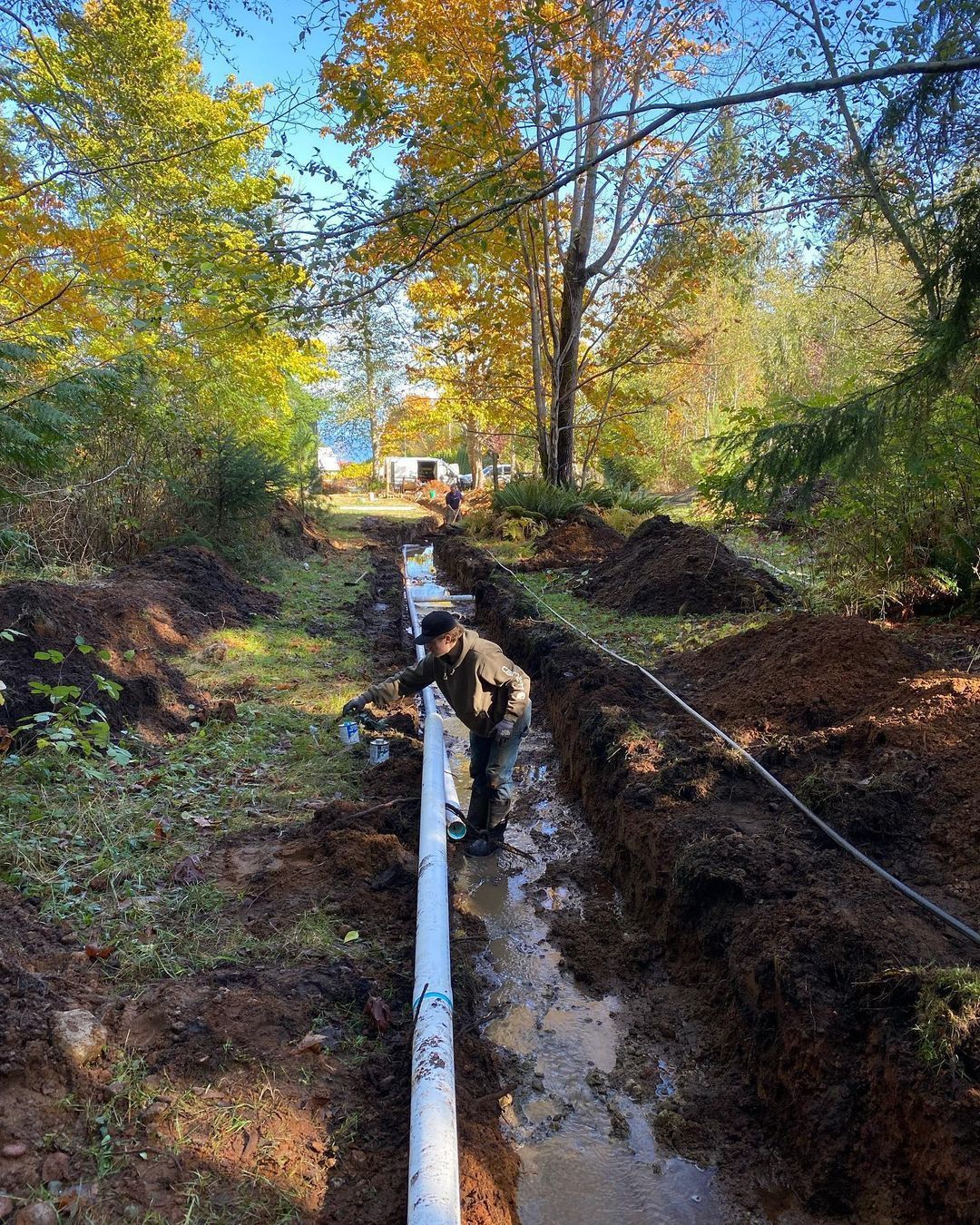 A man is working on a pipe in a muddy area.