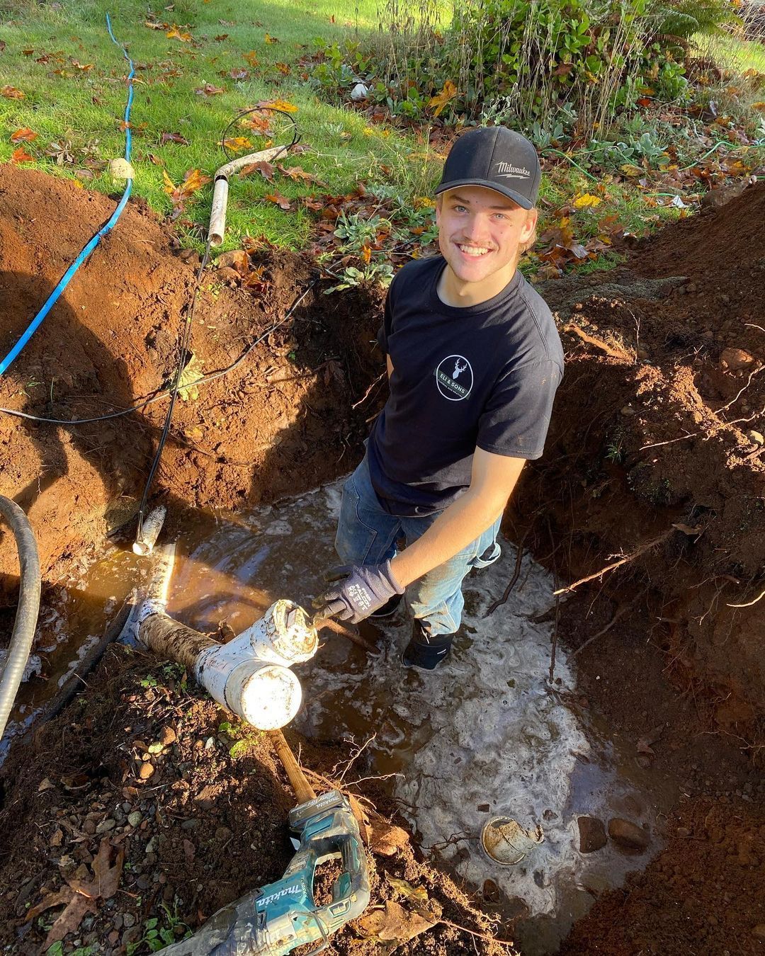 A man is kneeling in a muddy hole holding a shovel.