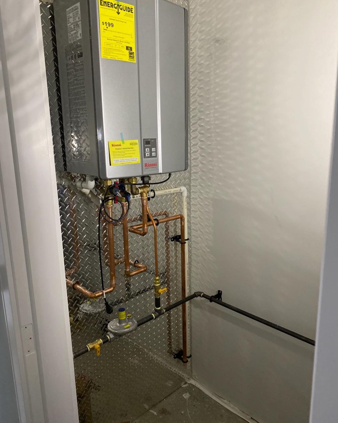 A water heater is sitting in a closet next to copper pipes.