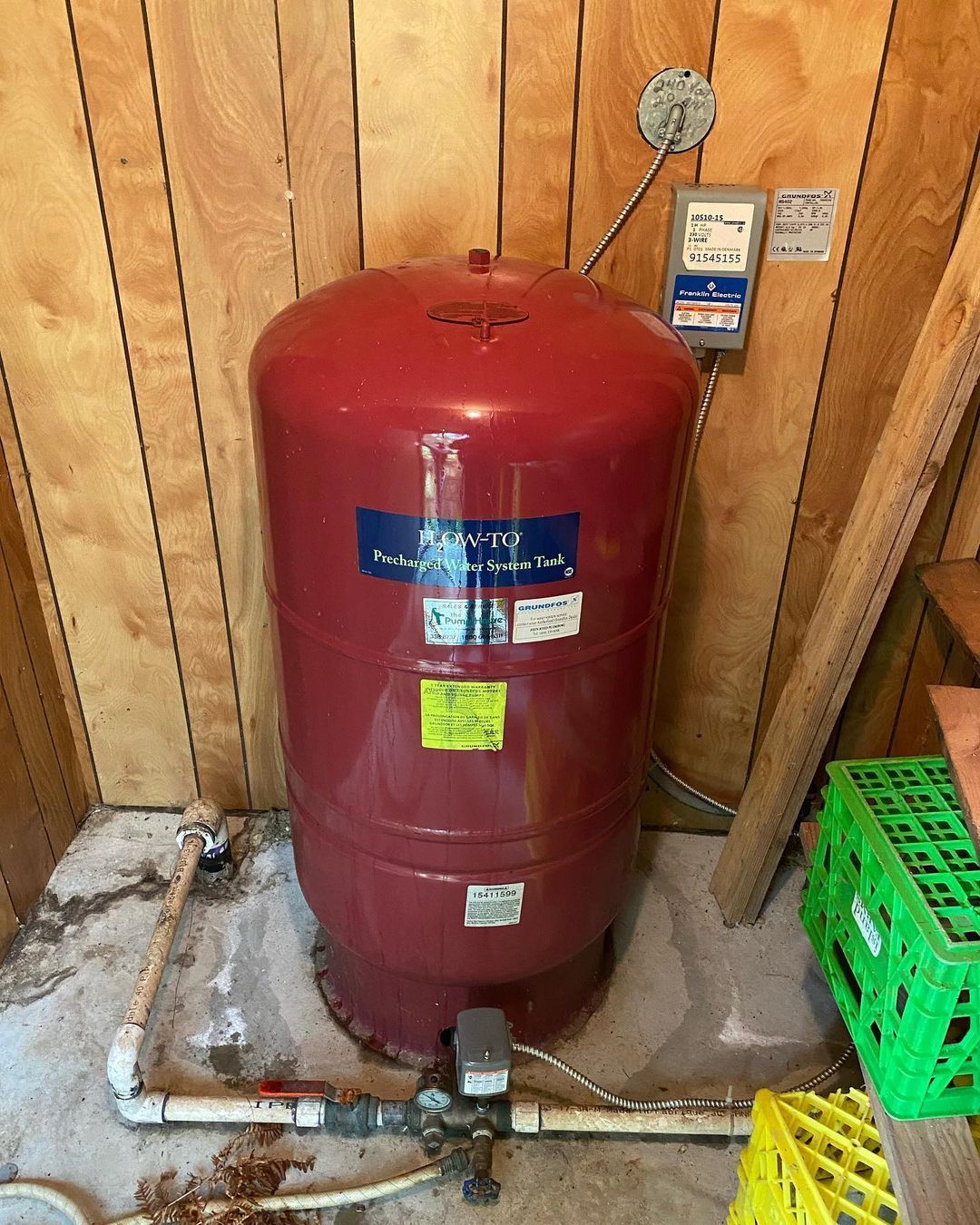 A red water tank is sitting in a room next to a wooden wall.