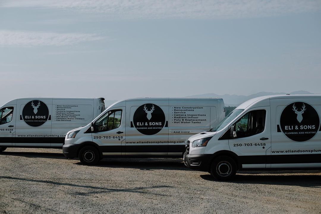 Three white vans are parked next to each other in a gravel lot.