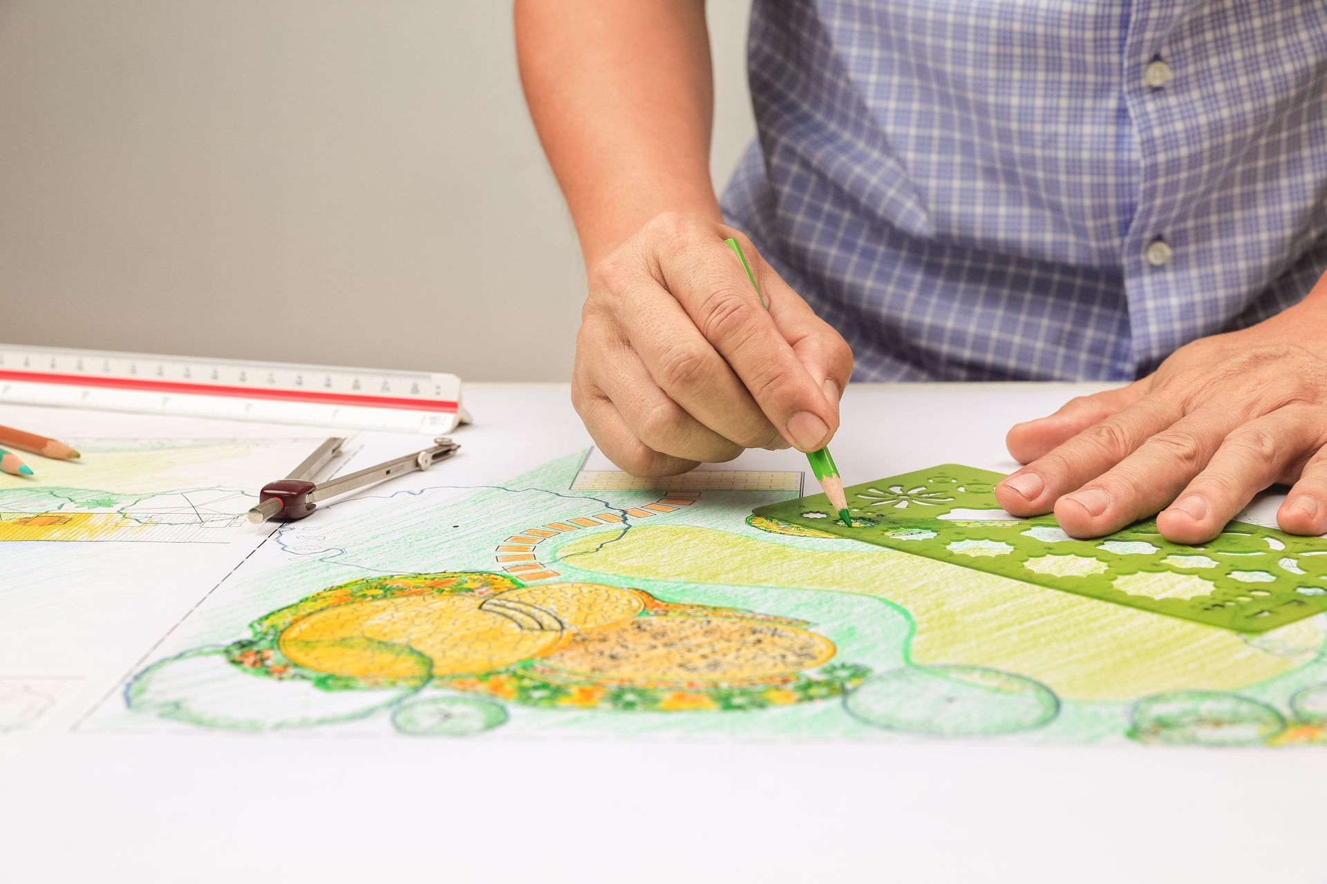 A close-up of a landscape designer working on a backyard garden plan with colored pencil.