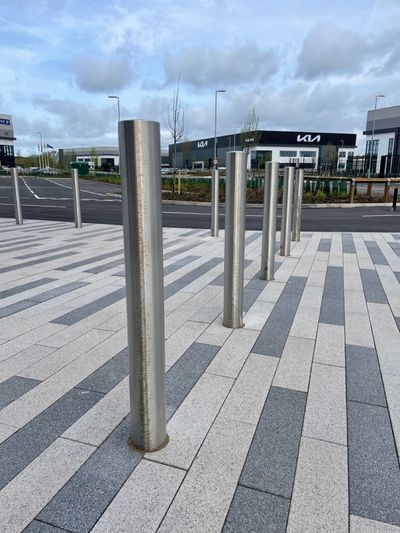 A row of stainless steel poles are lined up on a sidewalk.