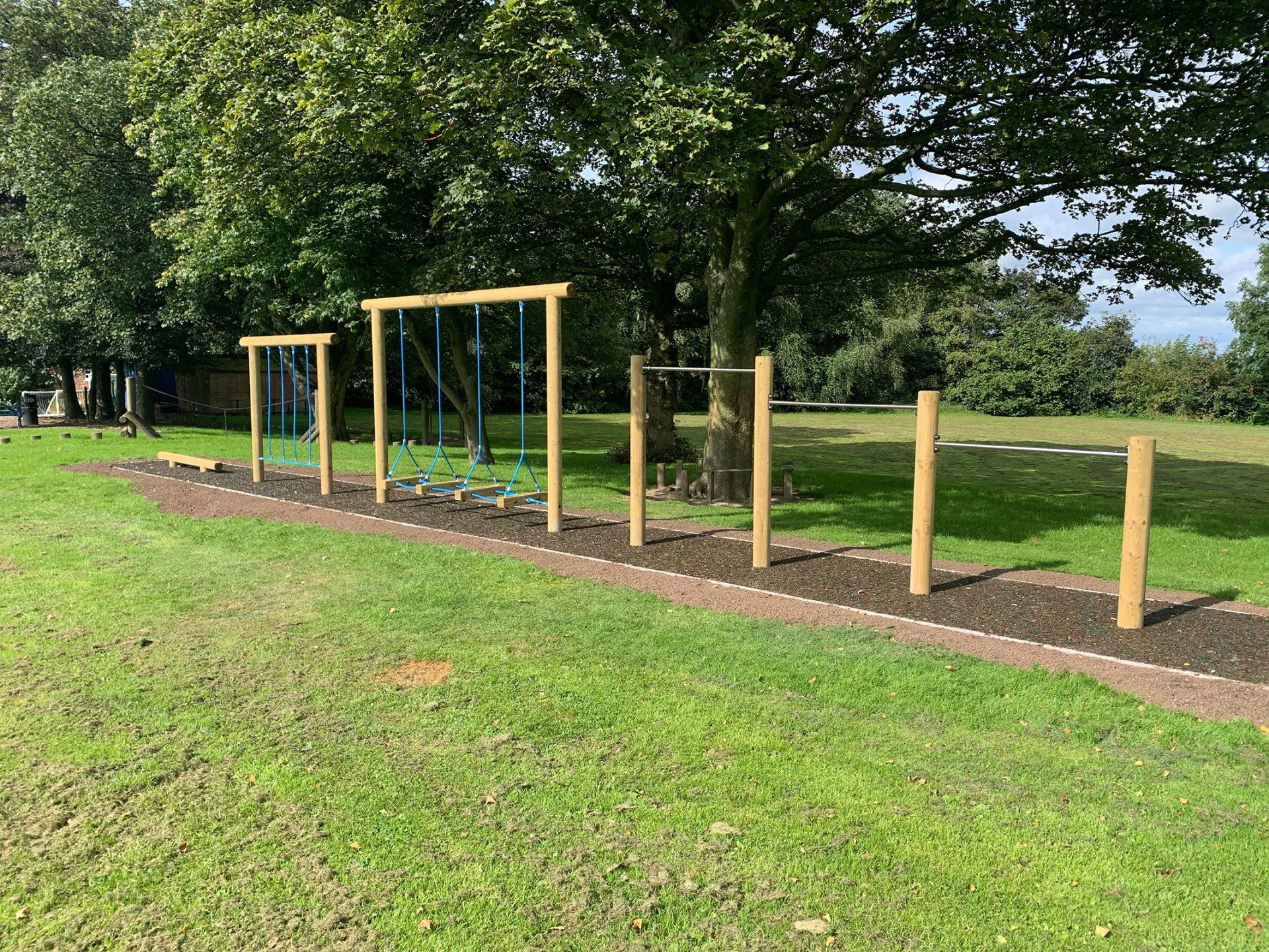 A row of wooden bars and swings in a park.