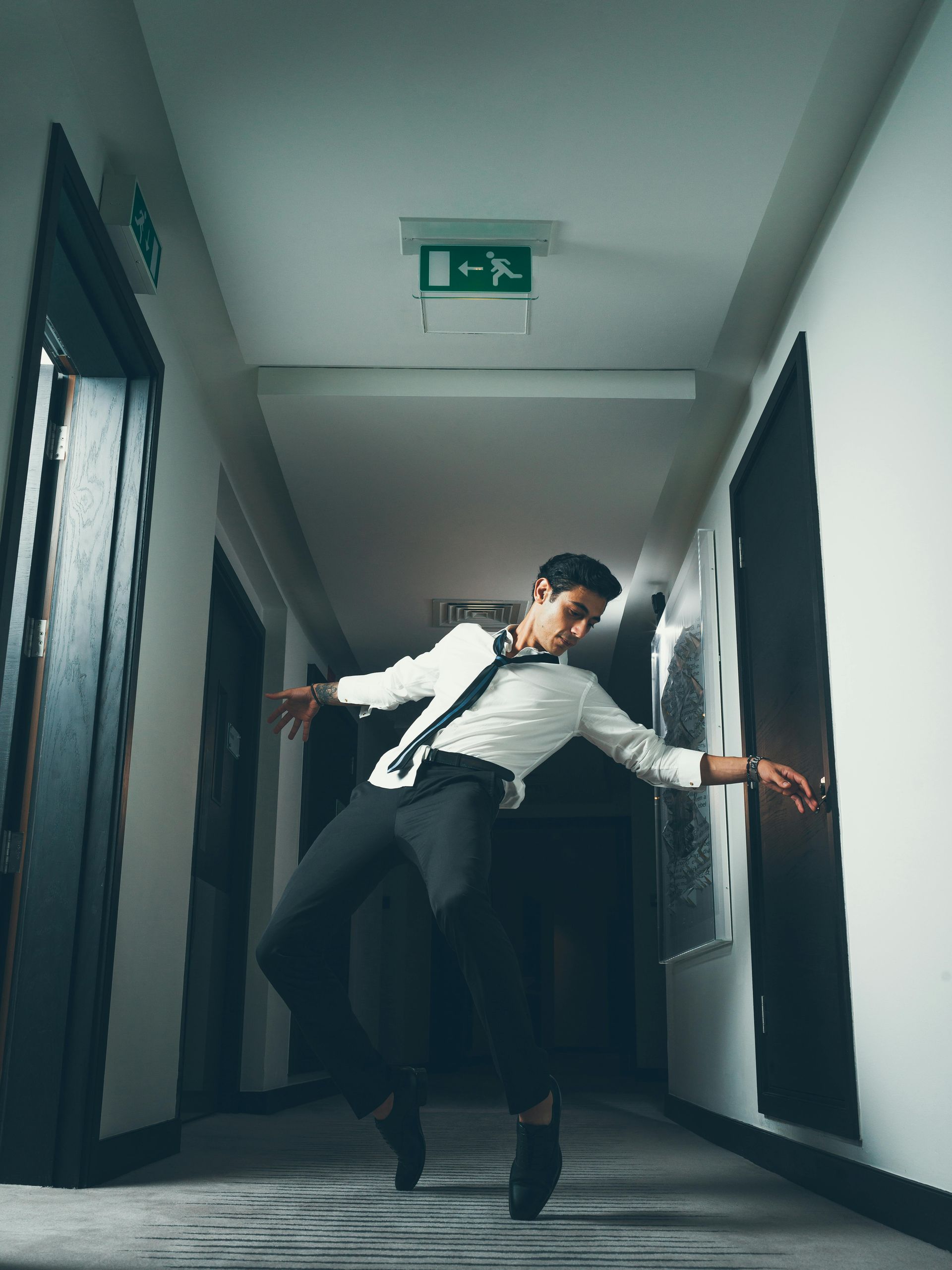 A man in a suit and tie is dancing in a hallway.