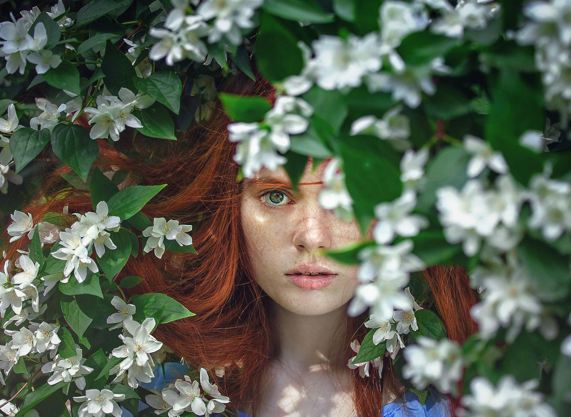 A woman with red hair is surrounded by white flowers and leaves.