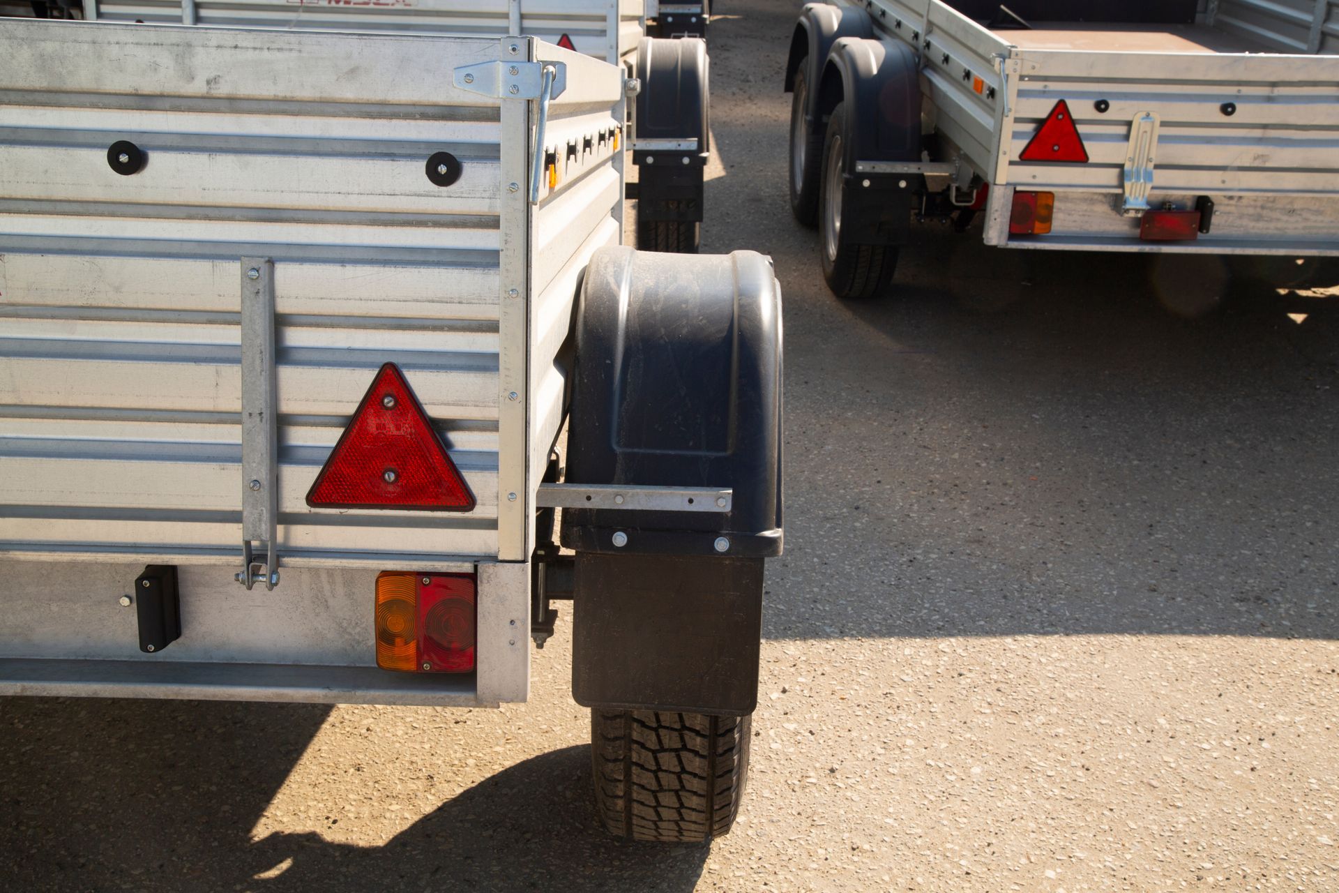 Silver utility trailers parked in a lot, with red reflectors and black tires visible.
