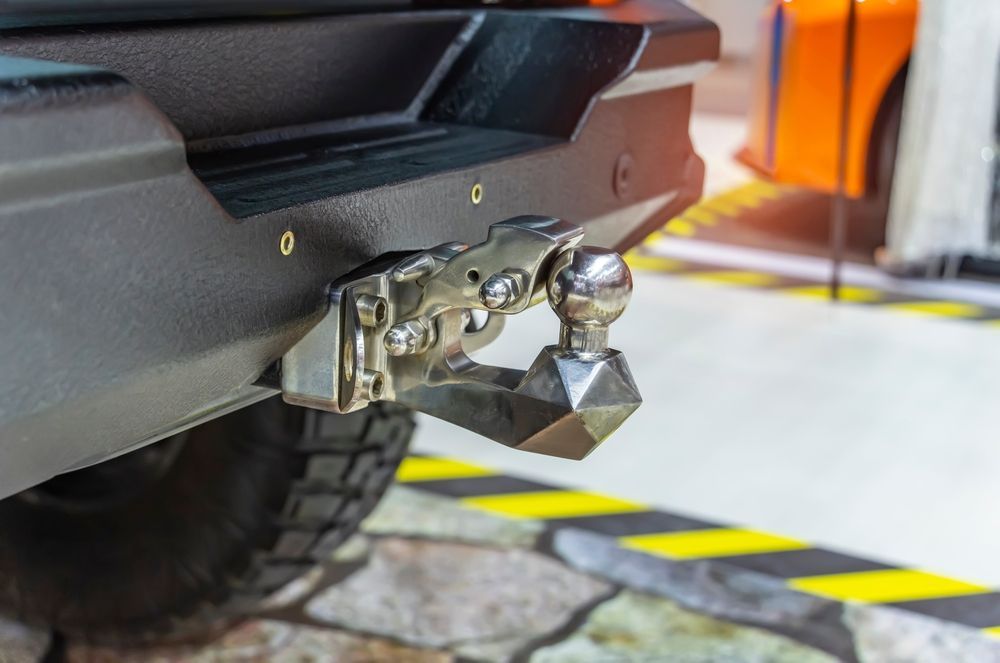 Close-up of a trailer hitch with shiny tow ball attached to a black vehicle bumper.