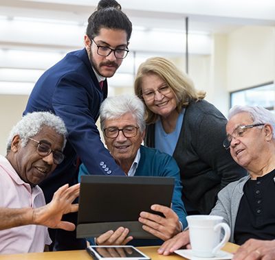A person in a business suit points to a digital tablet held by a group of people at a table, all looking at the screen.