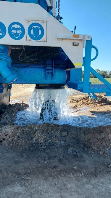Blue and White Drilling Machine Spurting Water Onto Dirt — Wilson's Drilling in South Kolan, QLD