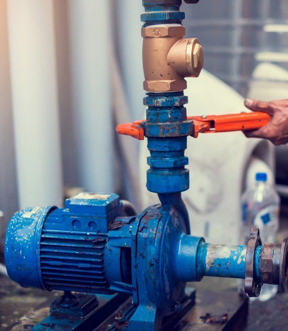 Plumber Using a Wrench on a Blue Pump With Copper and Blue Pipes — Wilson's Drilling in South Kolan, QLD