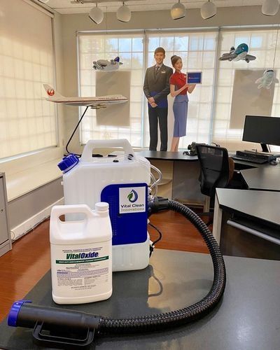 Indoor room with a fogging machine and cleaning supplies, with two people standing near a window.