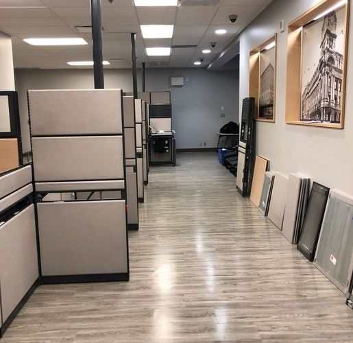 Office hallway with beige cubicles, framed art on the wall, and samples leaning against the right side.