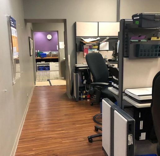 Office hallway with wood floor, cubicles, a desk chair, and a doorway to a purple-walled room