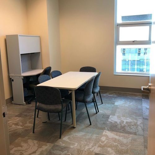 Small office meeting room with a white table, four chairs, and a cabinet by a window.
