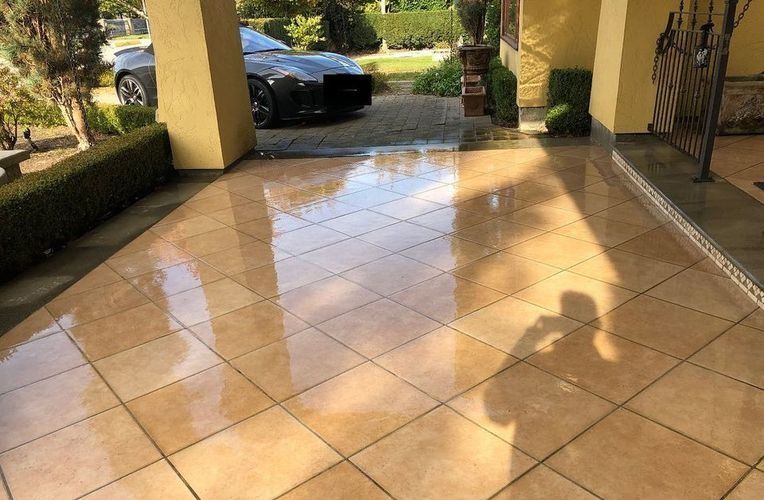 Sunlit tiled driveway and porch with a parked car and long shadows from nearby columns