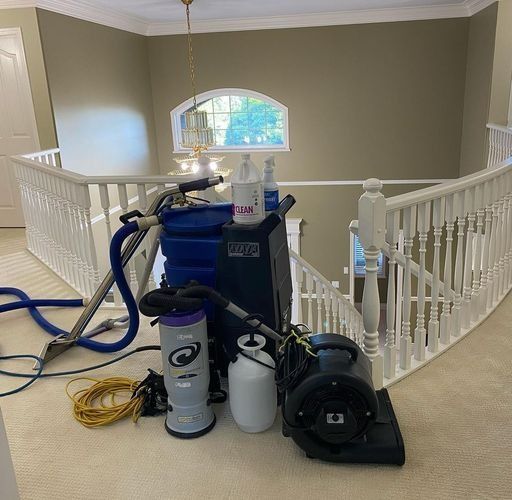 Cleaning equipment in a bright upstairs hallway beside a railing and arched window.