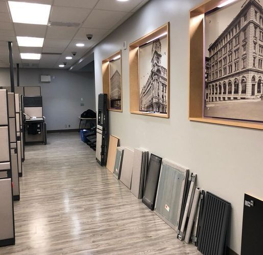 Hallway in a showroom with framed building prints and sample tiles leaning against the wall.