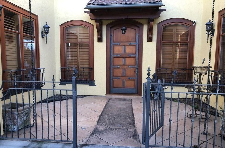 Front entrance with open iron gates, wooden door, and shuttered windows on a cream-colored house