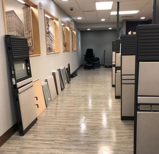 Office hallway with cubicle partitions, wall art, and stacked frames along a polished floor