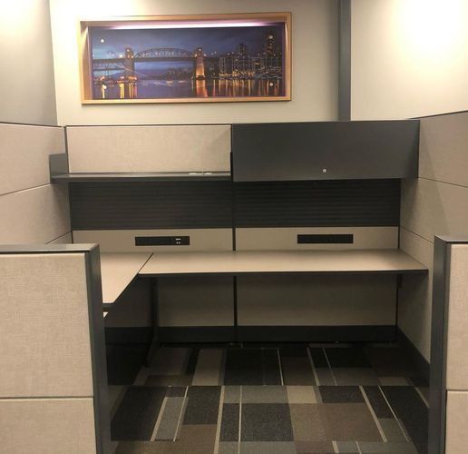 Empty office cubicle with beige partitions, dual desks, and a framed cityscape on the wall.