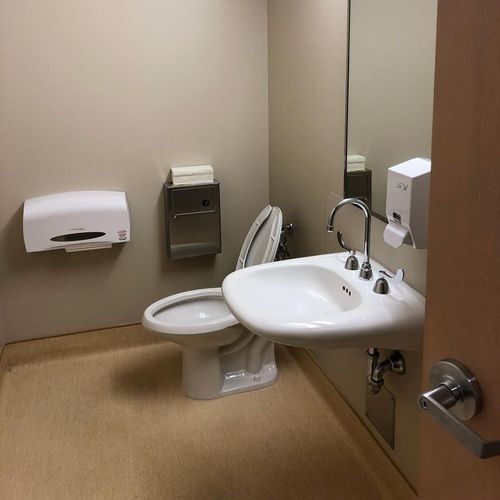 Accessible restroom with toilet, sink, grab bars, and wall-mounted dispensers in beige tones
