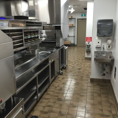 Commercial kitchen with stainless steel counters, ovens, sinks, and tiled floor.