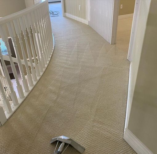 Carpeted upstairs hallway with white railing and beige walls; a small gray object lies on the floor.