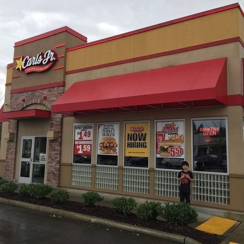 Carl’s Jr. storefront with red awnings, promotional posters, and a person standing outside on a rainy sidewalk