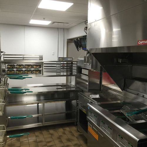 Commercial kitchen with stainless steel counters, shelves, and a large range hood