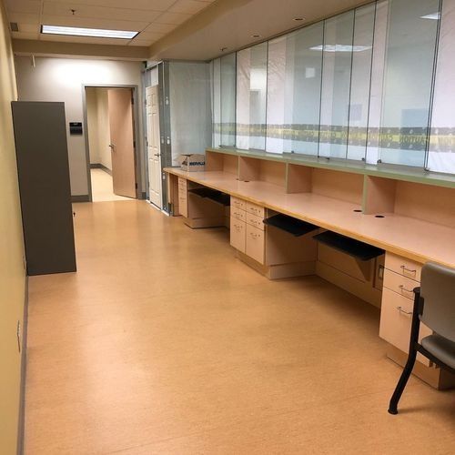 Empty office hallway with wooden desks, glass partitions, and tan flooring
