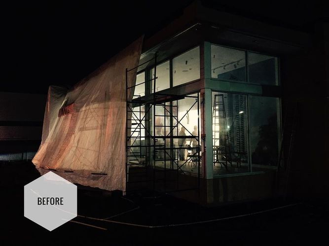 Nighttime view of a glass-walled building under construction, with a tarp draped over one side and a “BEFORE” label.