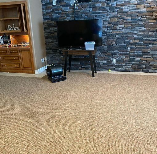 Living room with carpet, stone fireplace wall, TV, small table, and wooden cabinet