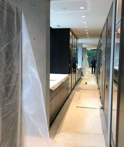 Narrow hallway with glass walls, white cabinets, and a plastic-covered area under renovation.