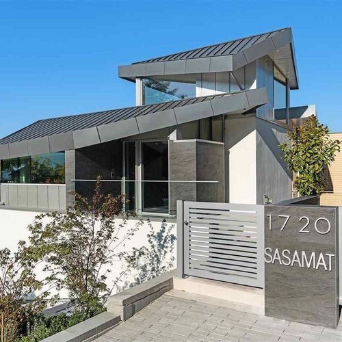 Modern house exterior with angular rooflines, glass windows, and a gray gate labeled 1720 SASAMAT.
