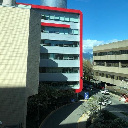 Red-outlined modern office building beside a parking lot under a blue sky