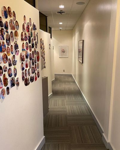 Narrow office hallway with carpet, framed wall art, and a colorful collage of circular photos on the left wall