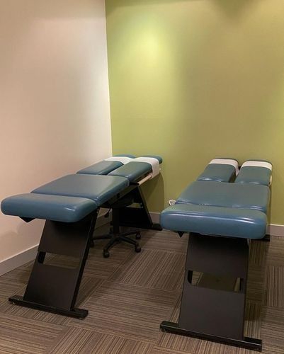 Two blue padded treatment tables in a small exam room with green and beige walls.