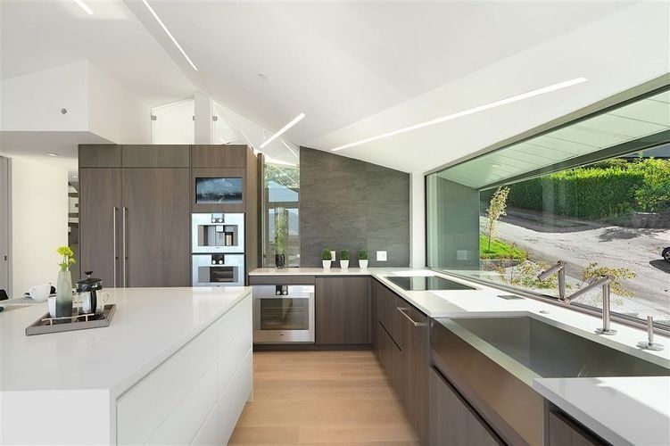 Modern white kitchen with dark wood cabinets and a large window overlooking greenery