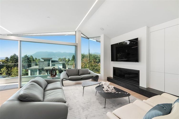Modern living room with gray sectional, fireplace, wall TV, and panoramic ocean-view windows